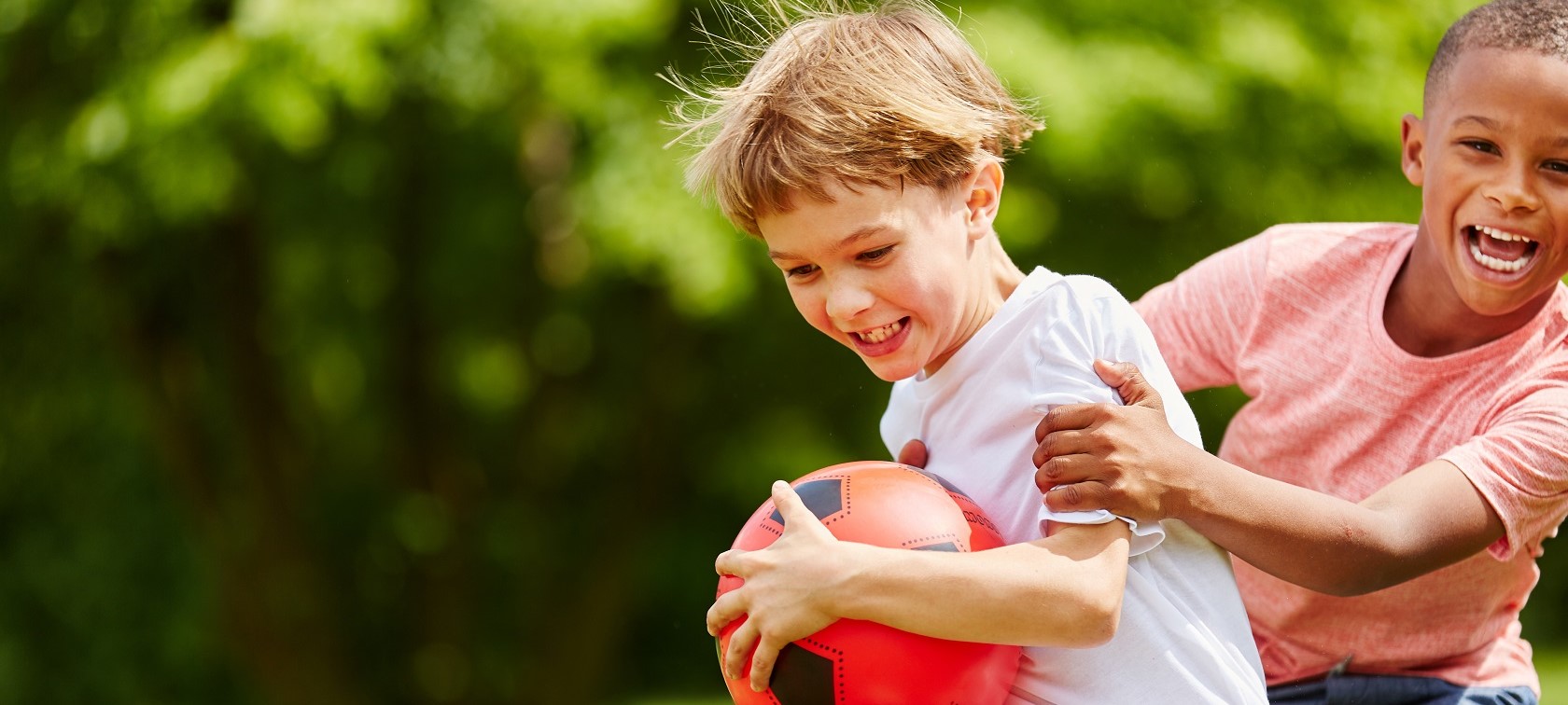 BKK STARKE KIDS. 2 junge lachende Kinder spielen mit einem roten Plastikball in der Hand.